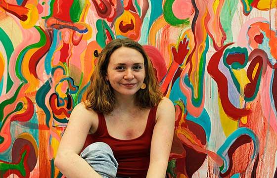 smiling woman sitting in front of large colorful painting