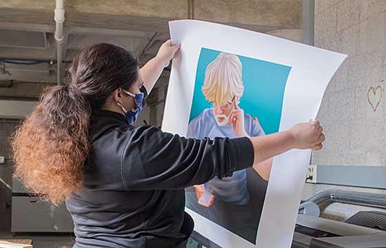 Jordyn stands holding up a large print, back to camera, gray sweatshirt, hair in ponytail