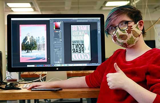 Ten sitting at computer with red shirt and mask showing thumbs up