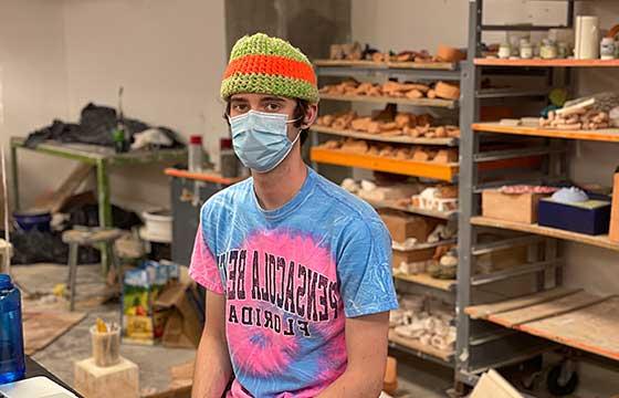 Colin sitting in studio with orange and green beanie, mask and blue and pink tie die shirt