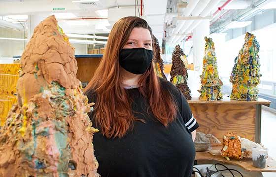 Bri standing in black mask beside a life sized ceramic sculpture