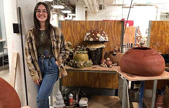 Caile standing in studio to the right of a studio table with large terra cotta sculpture